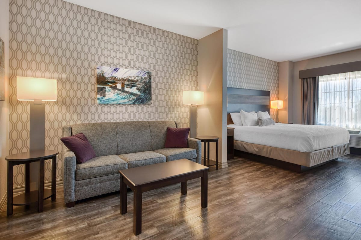 A hotel room with a patterned wallpaper, a large bed, a sofa, a coffee table, and two side tables with lamps.