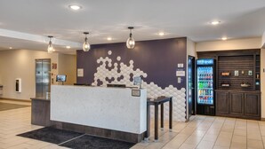 A reception area with a marble counter, a wall-mounted hexagonal pattern, a beverage dispenser, and a digital screen. - Best Western Plus Saint Peter (Saint Peter)