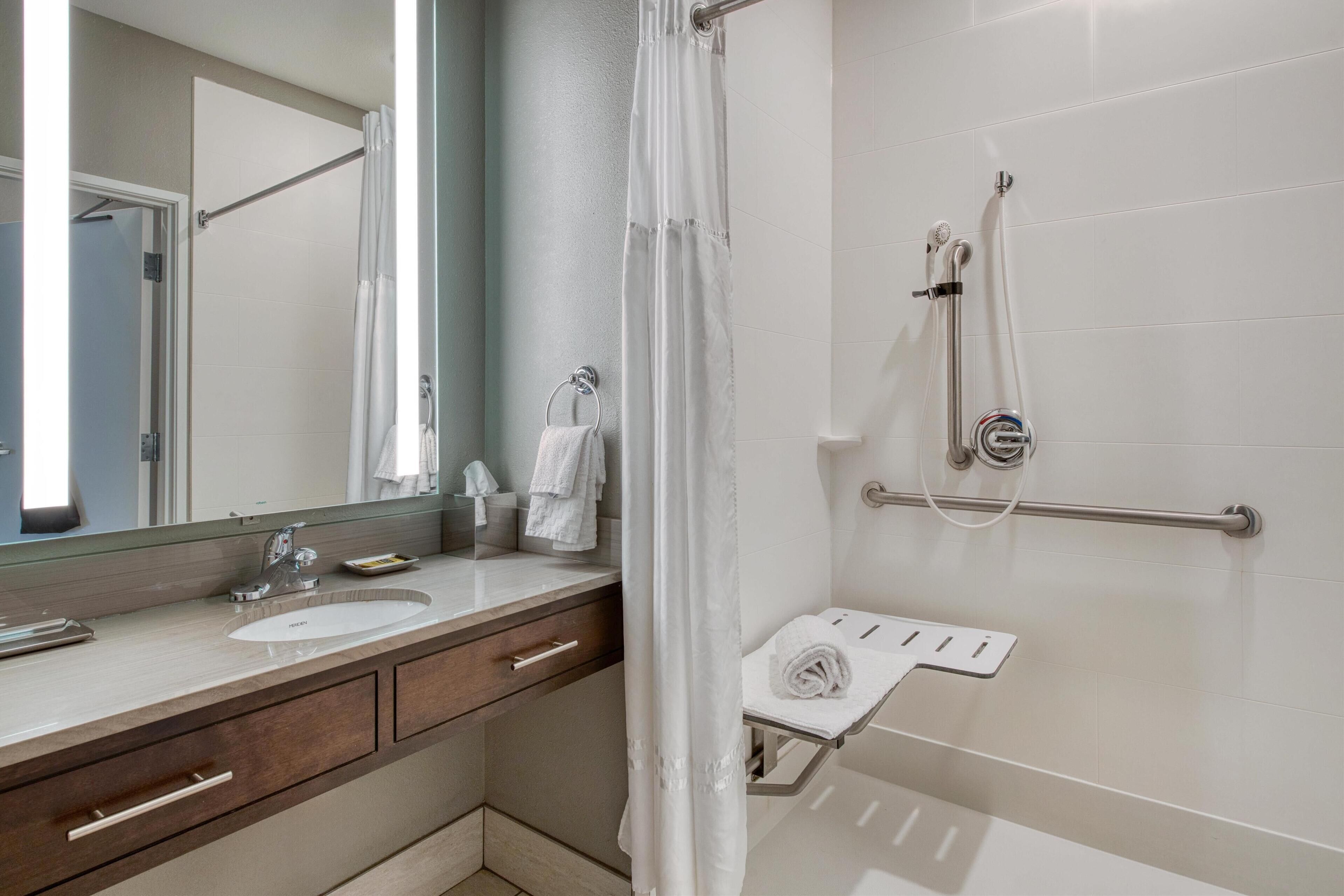 Un baño moderno con un espejo grande, un lavamanos, una ducha con cabezal de ducha manual y un perchero para toallas.
