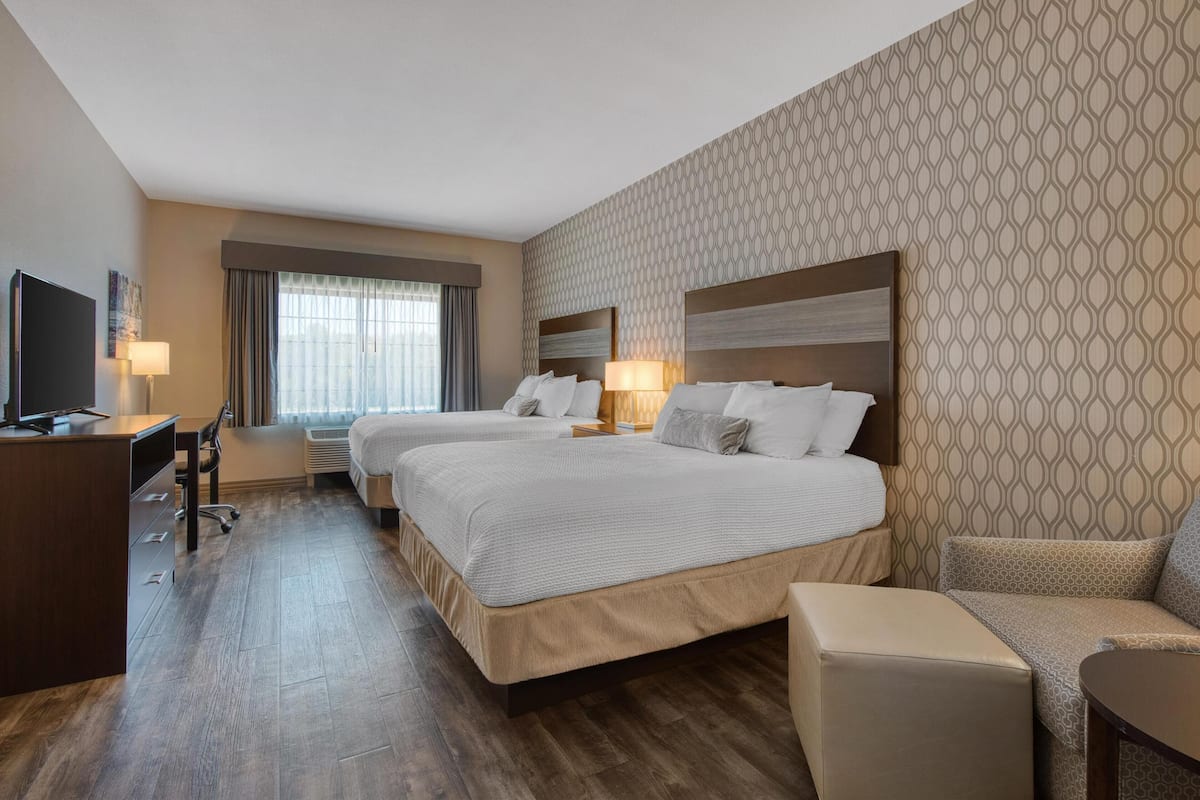 A hotel room with two beds, a desk, a chair, and a TV.