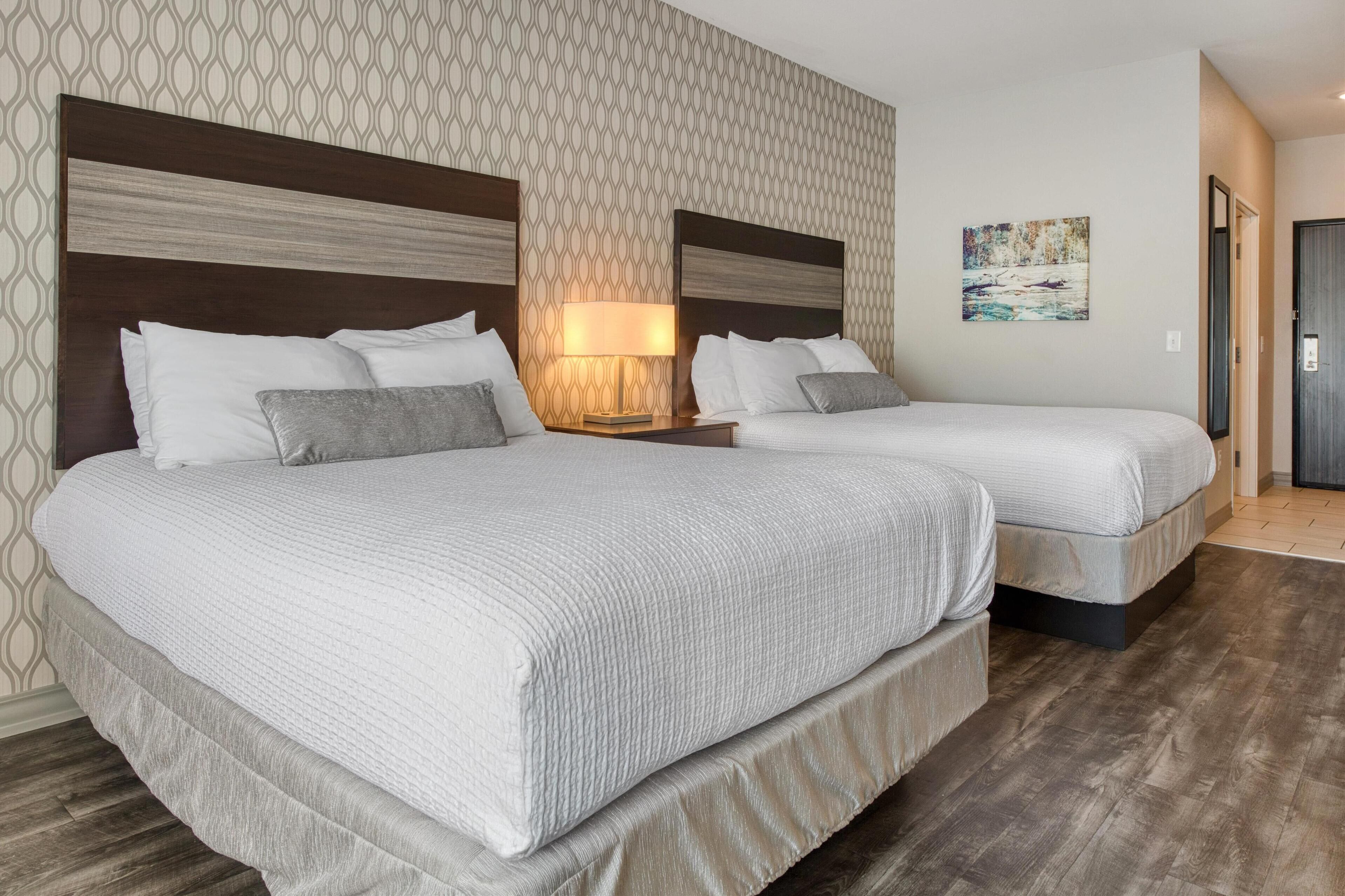 Une chambre d’hôtel avec deux lits, une table de chevet avec une lampe, un papier peint à motifs et un tableau au mur.