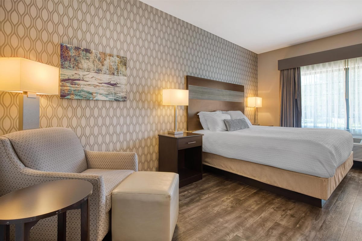 A hotel room with a patterned wallpaper, a bed with white bedding, a sofa, a small table, and two bedside lamps.