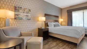 Una habitación de hotel con papel tapiz estampado, una cama con ropa de cama blanca, un sofá, una mesita y dos lámparas de noche.