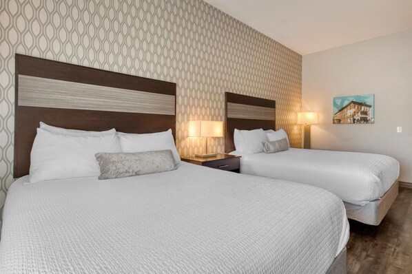 A hotel room with two beds, a patterned wallpaper, a nightstand with a lamp, and a painting on the wall. - Best Western Plus Saint Peter (Saint Peter)