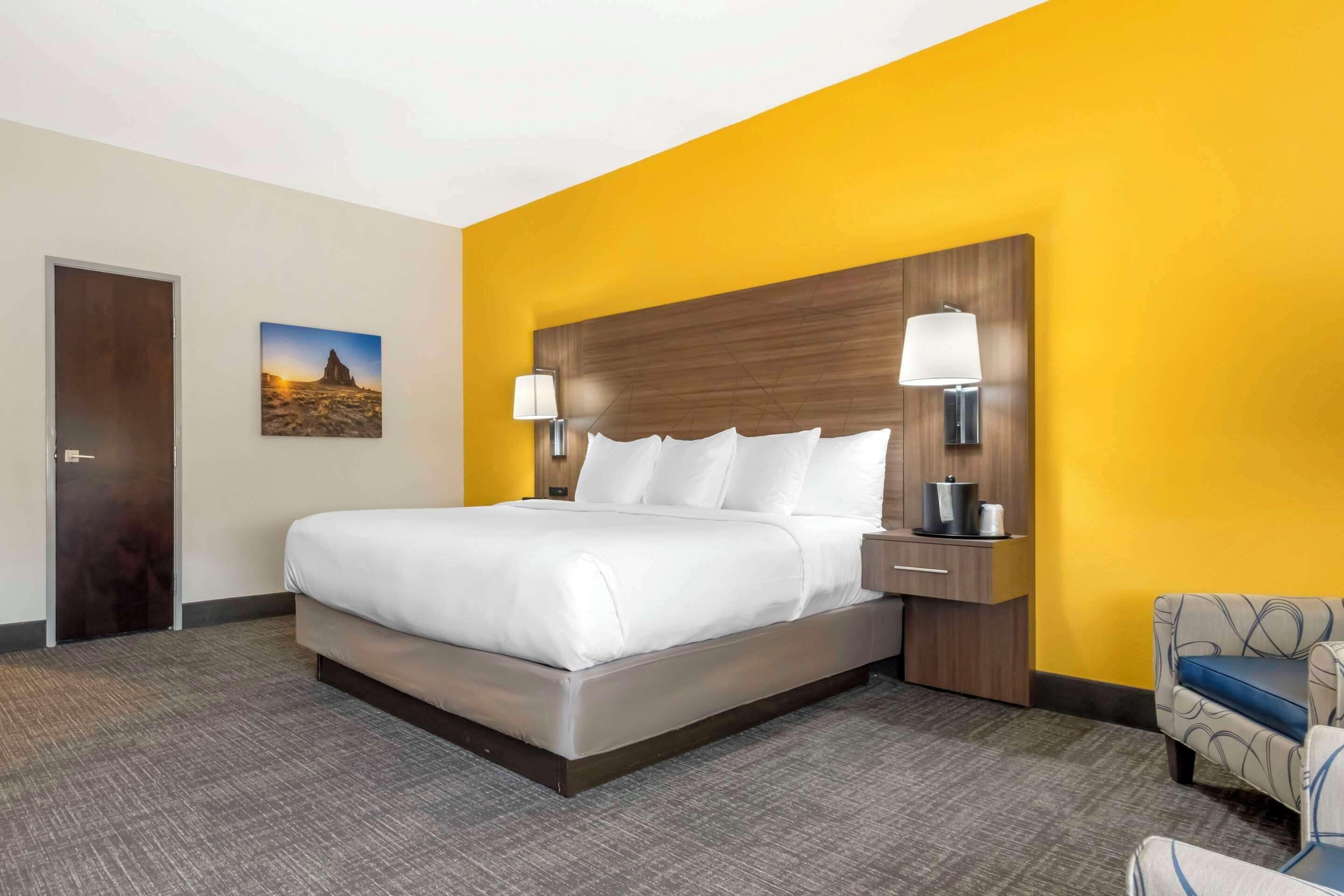Camera d'albergo con un letto grande, un comodino con una lampada, una sedia e un quadro appeso al muro.