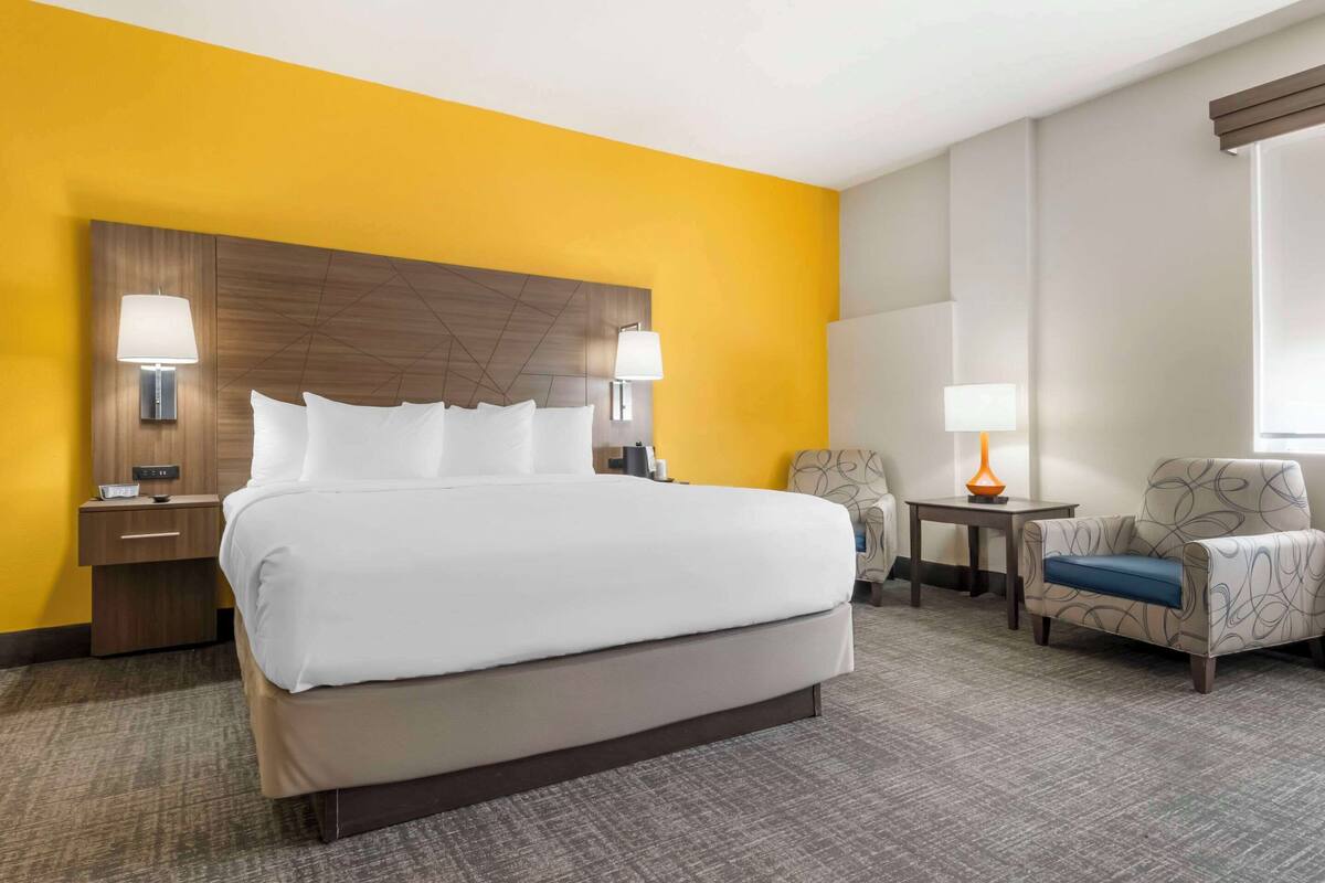 A hotel room with a large bed, two bedside tables with lamps, a chair, and a small table with a lamp.