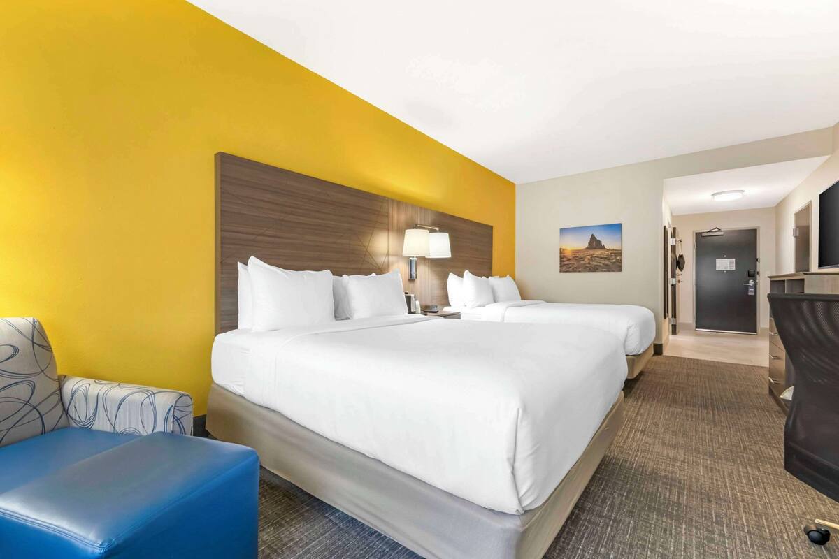 A hotel room with two beds, a desk, a chair, and a lamp.