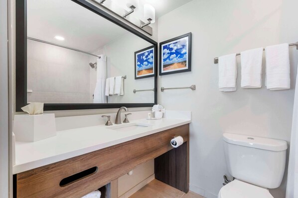 A modern bathroom with a white sink, a large mirror, and a toilet. There are towels hanging on a rack and a framed picture on the wall.