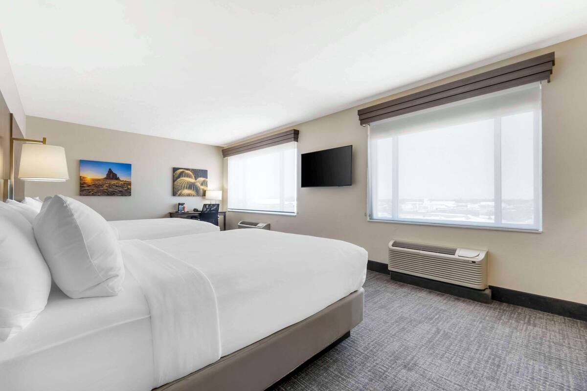 A hotel room with a large bed, a desk, a flat-screen TV, and a window with a city view.