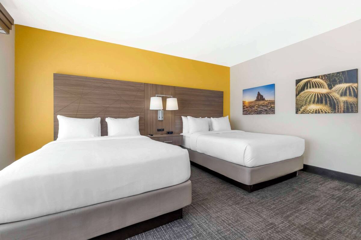 A hotel room with two beds, a wooden headboard, two bedside lamps, and two wall-mounted paintings.