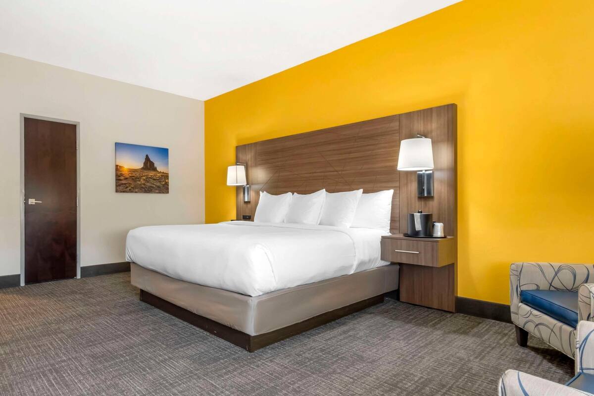 A hotel room with a large bed, bedside lamps, a nightstand, and a chair.