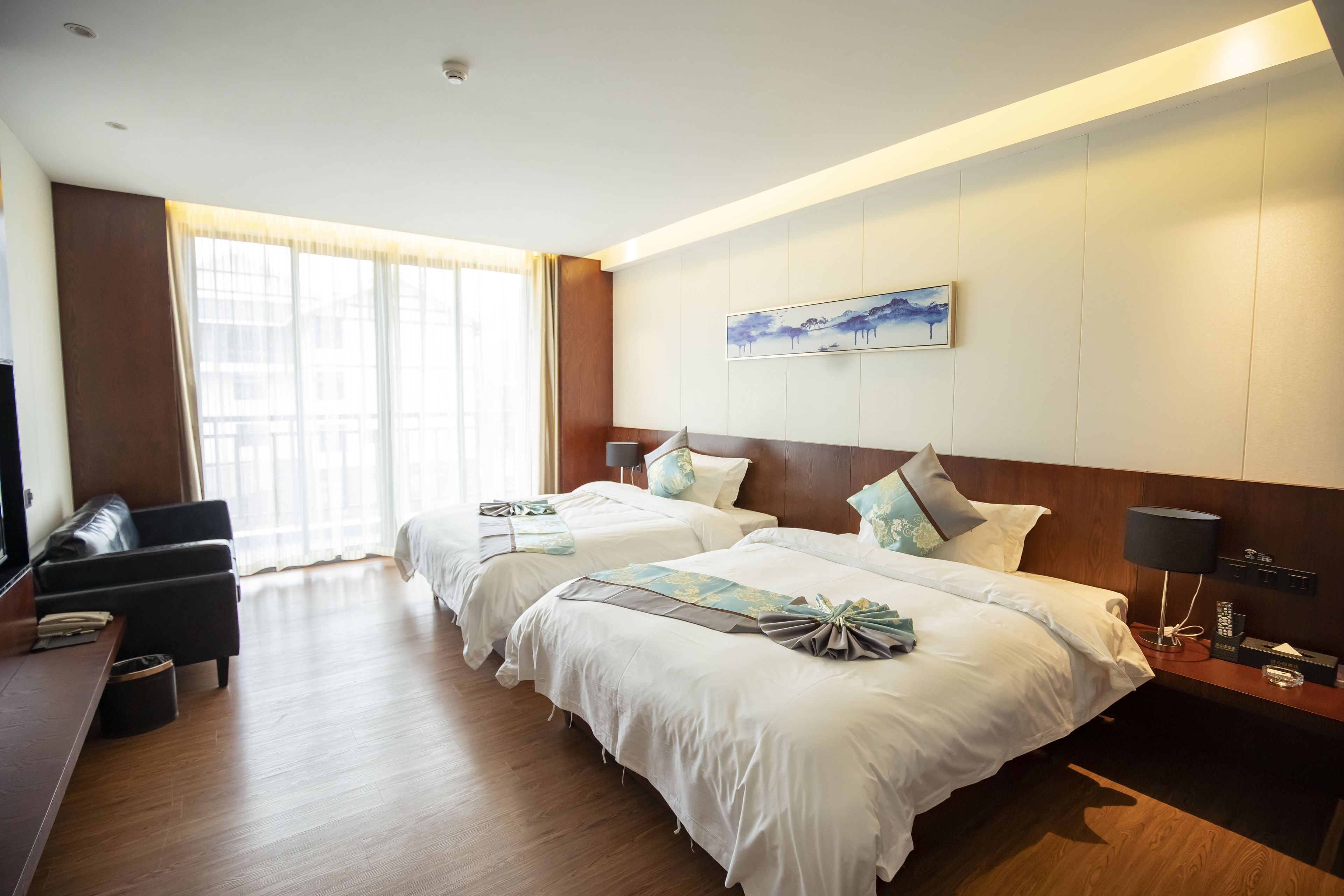 Quarto de hotel com duas camas, uma mesa, uma cadeira, uma televisão e uma janela com cortinas.