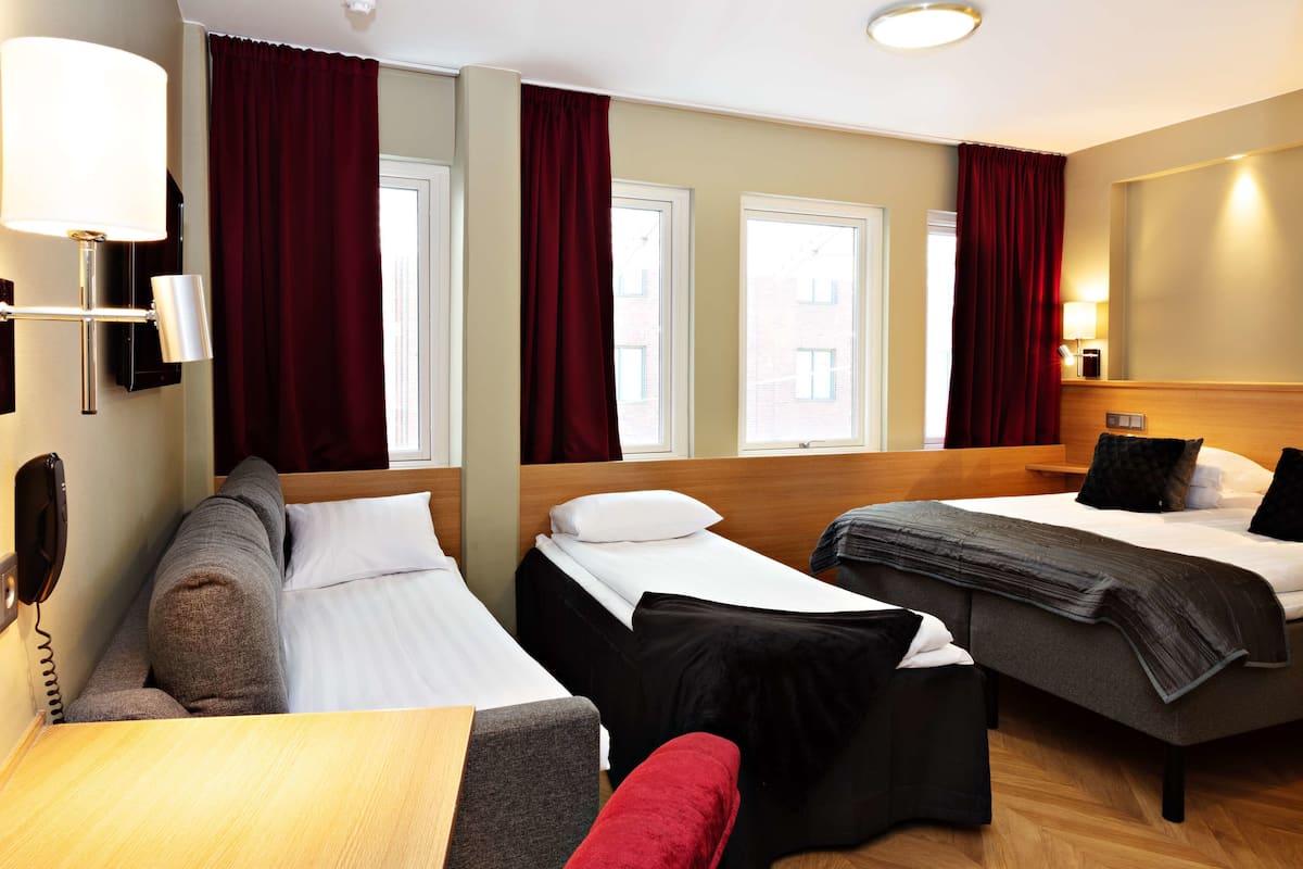 A hotel room with two beds, a sofa, a table, and a lamp.