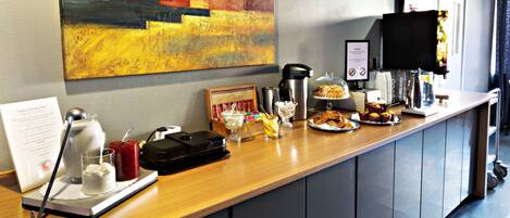 A hotel reception area with a coffee station, a painting on the wall, and a sign with room information.