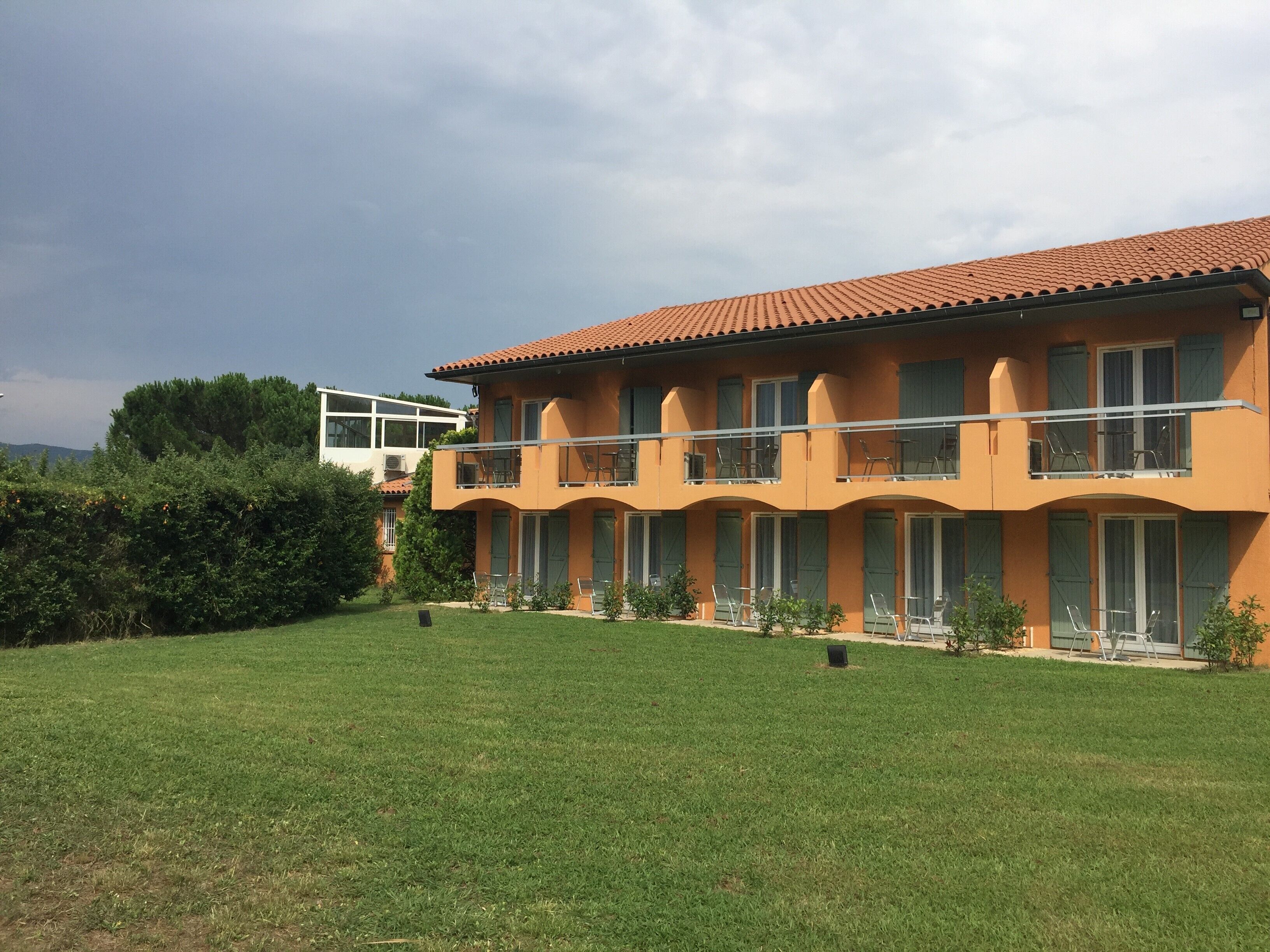 Een gebouw met twee verdiepingen, een dak met rode tegels, meerdere balkons met stoelen en een verzorgd gazon.