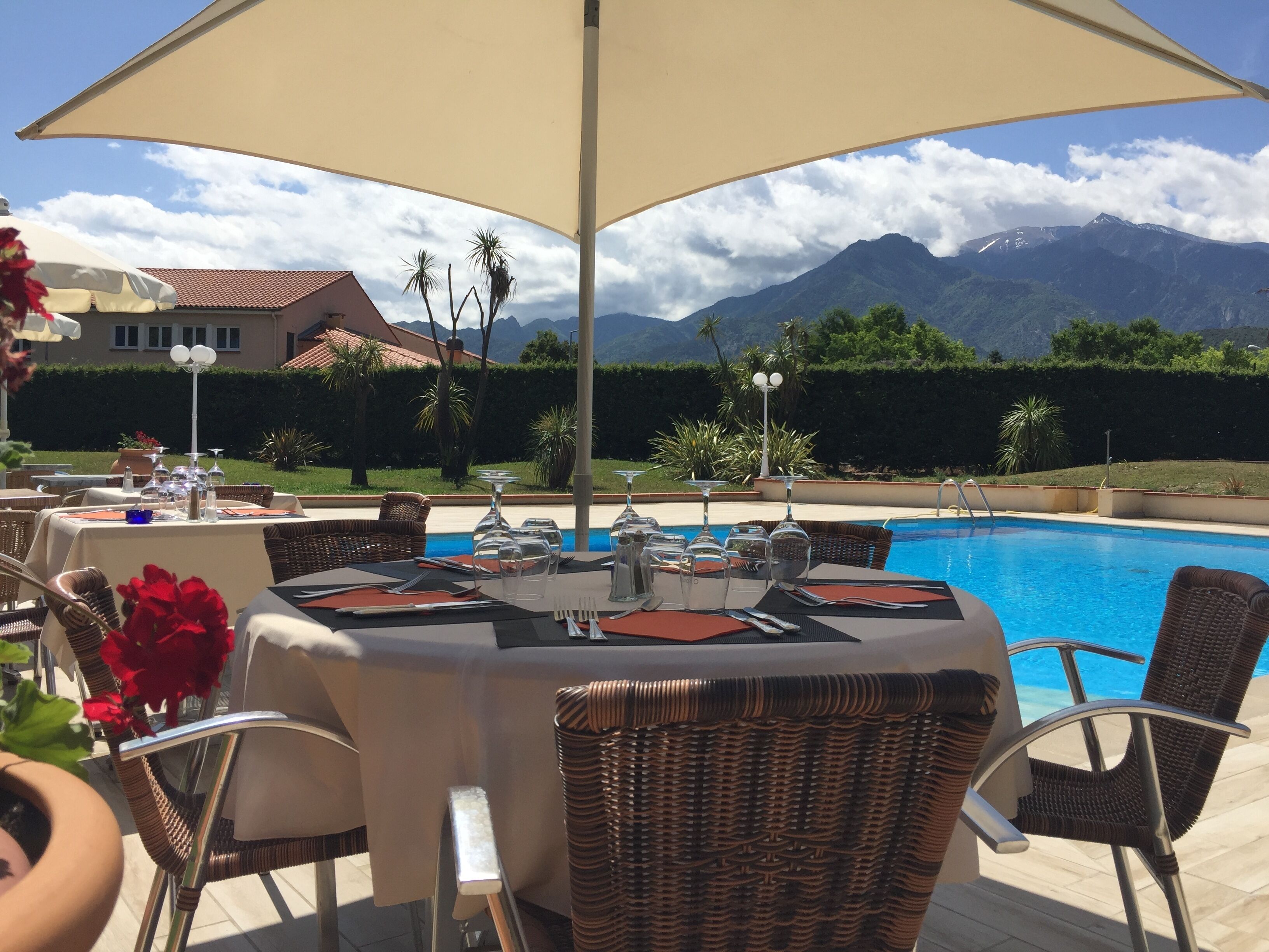 Un área de comedor al aire libre con mesas dispuestas para una comida, con vista a una piscina y montañas.