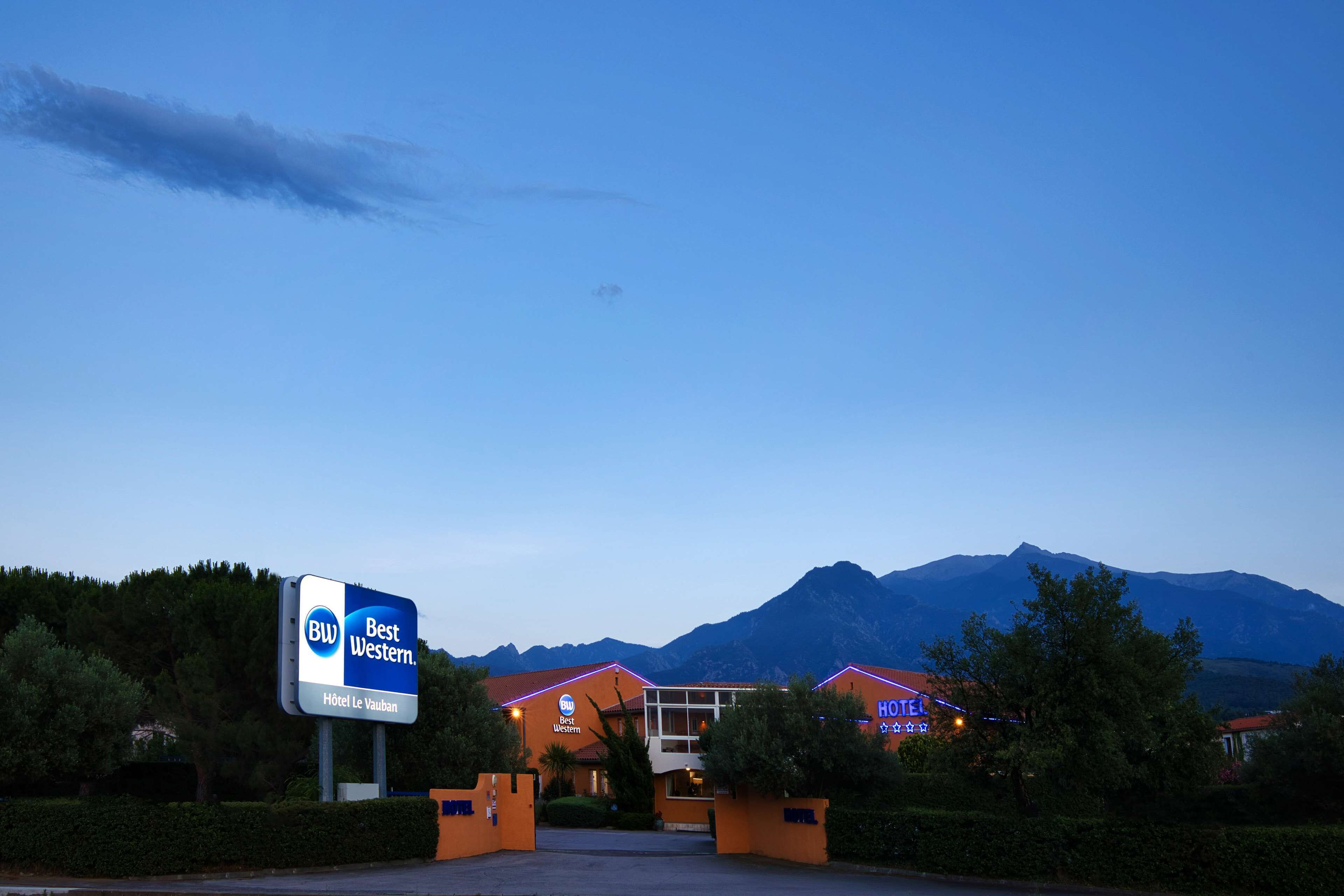 A hotel named Best Western with a signboard, surrounded by greenery and mountains in the background.