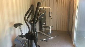 A gym with exercise equipment including a NordicTrack elliptical, a bench, and a weight machine.