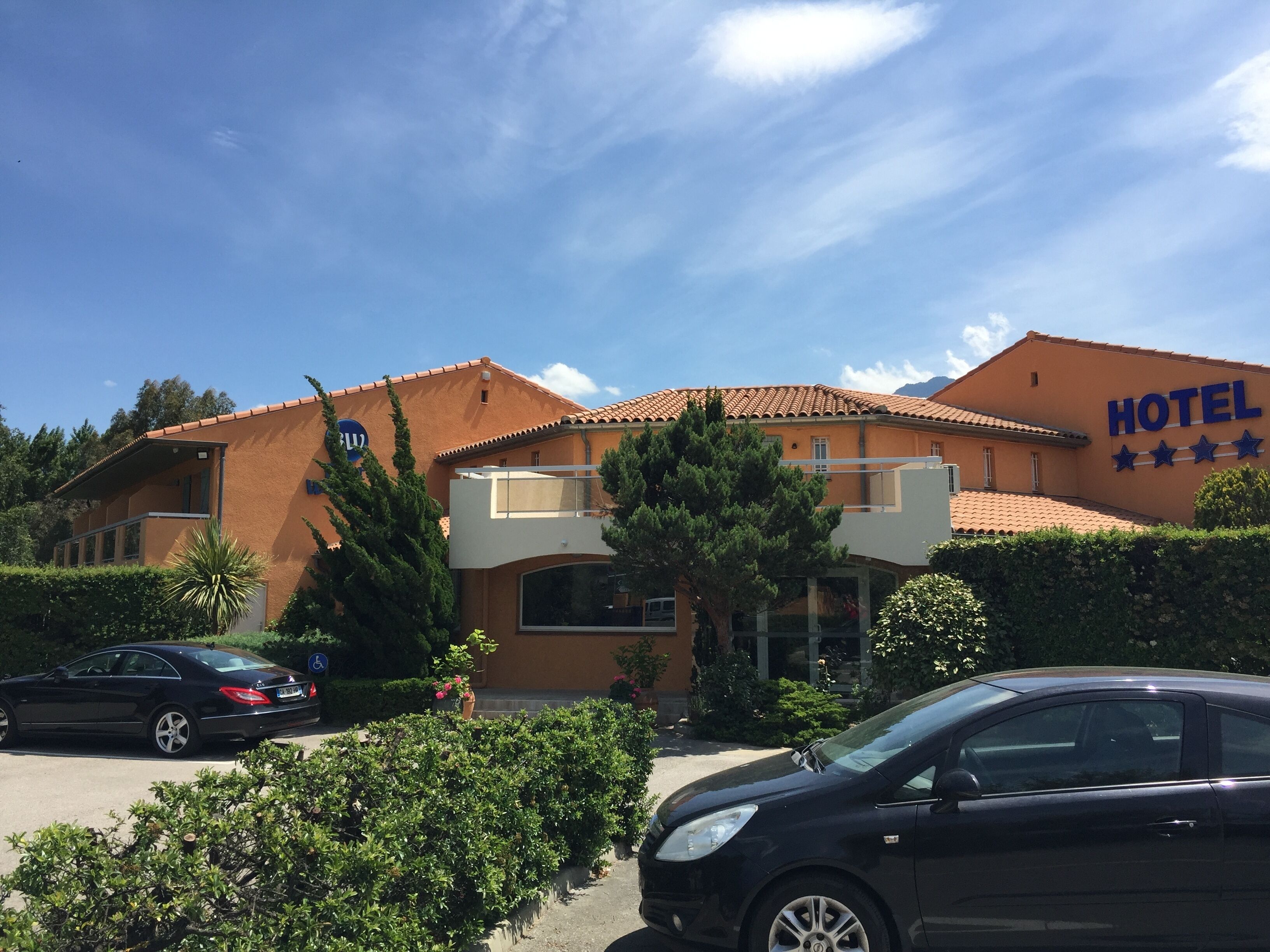 Un hôtel avec une enseigne indiquant un classement cinq étoiles, un espace de stationnement et un ciel d’un bleu limpide.
