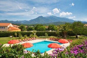 A swimming pool with red umbrellas, lounge chairs, and a mountain backdrop.