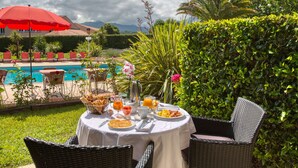 An outdoor dining area with a table set for breakfast, overlooking a swimming pool and lush greenery. - Best Western Le Vauban (Prades)