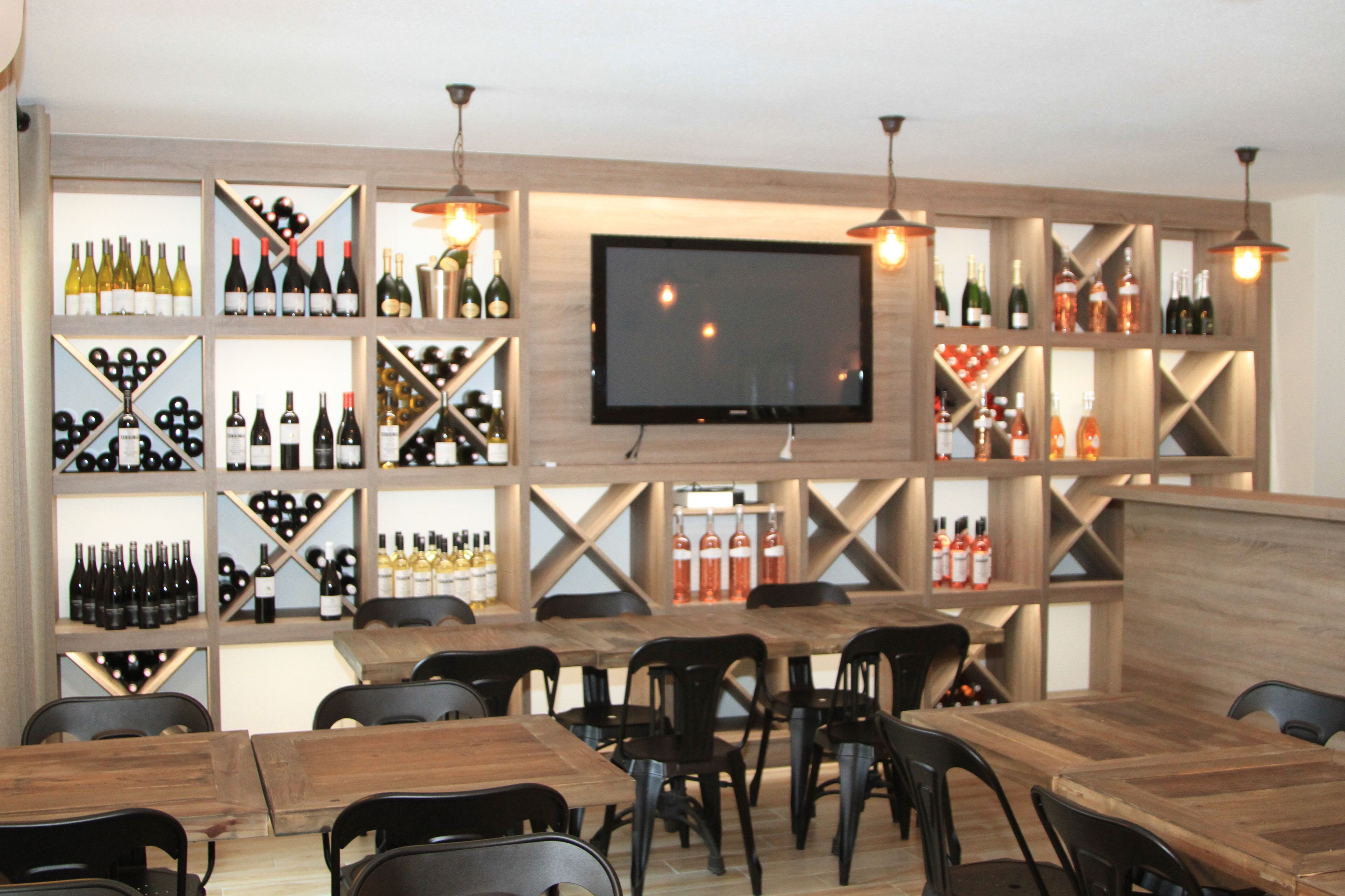 Zona de bar con estantes de madera que exhiben varias botellas, un televisor de pantalla plana y varias mesas y sillas.