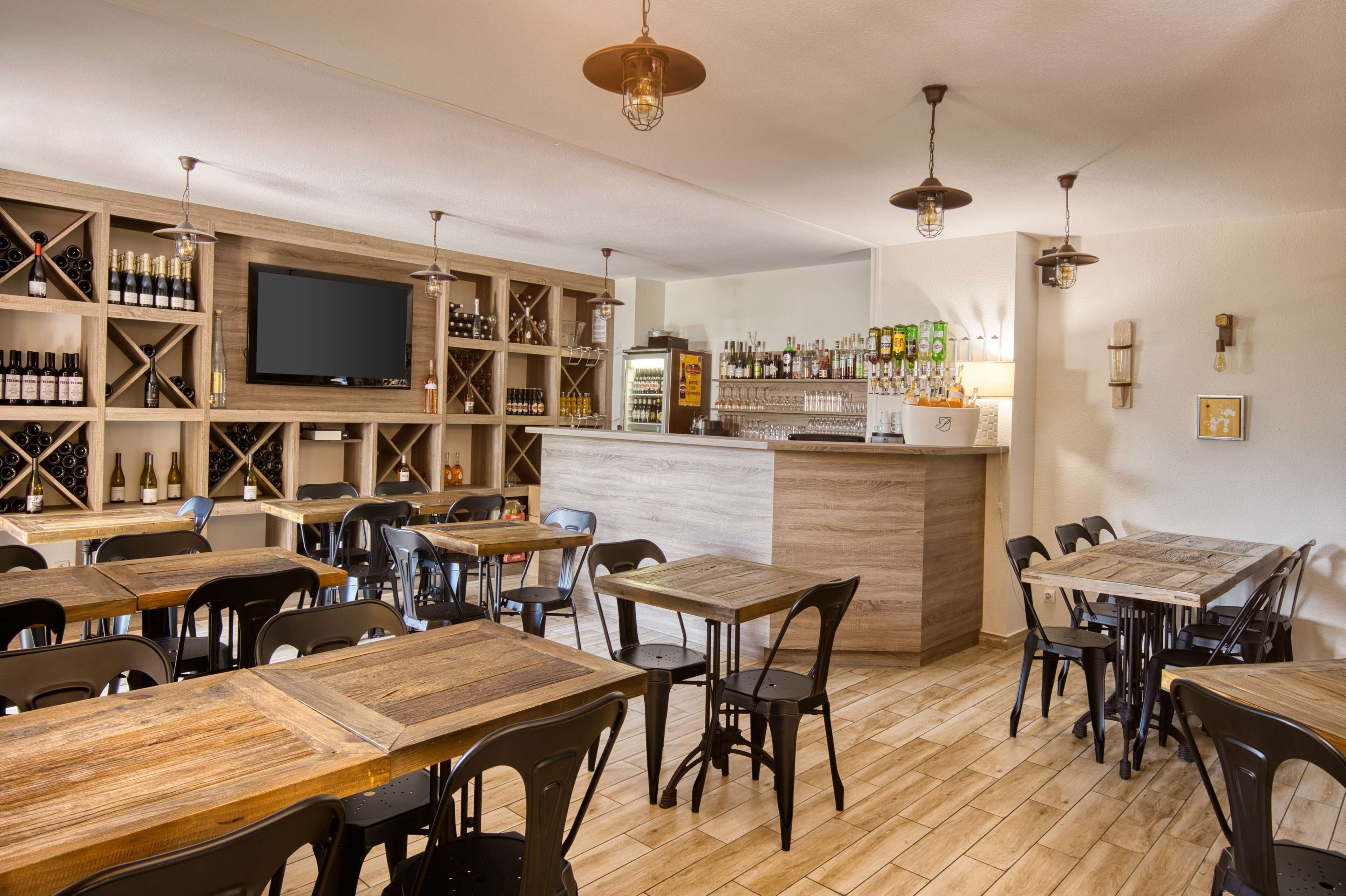 A restaurant with wooden tables and chairs, a bar area with a TV, and wine bottles on shelves.