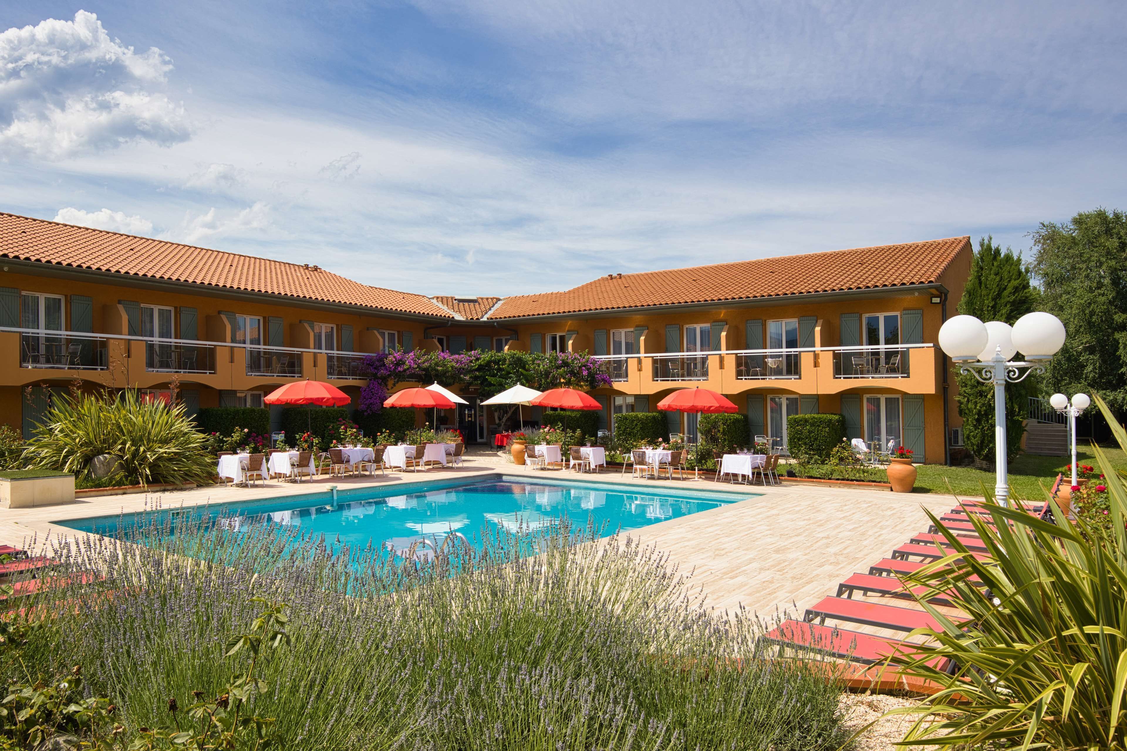 Ett hotell med en swimmingpool, utomhusmöbler och röda parasoller.