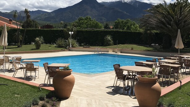 A swimming pool with lounge chairs and tables, surrounded by a landscaped garden and a mountain backdrop. - Best Western Le Vauban (Prades)