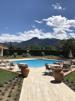 A swimming pool with lounge chairs and tables, surrounded by a landscaped garden and a mountain backdrop. - Best Western Le Vauban (Prades)