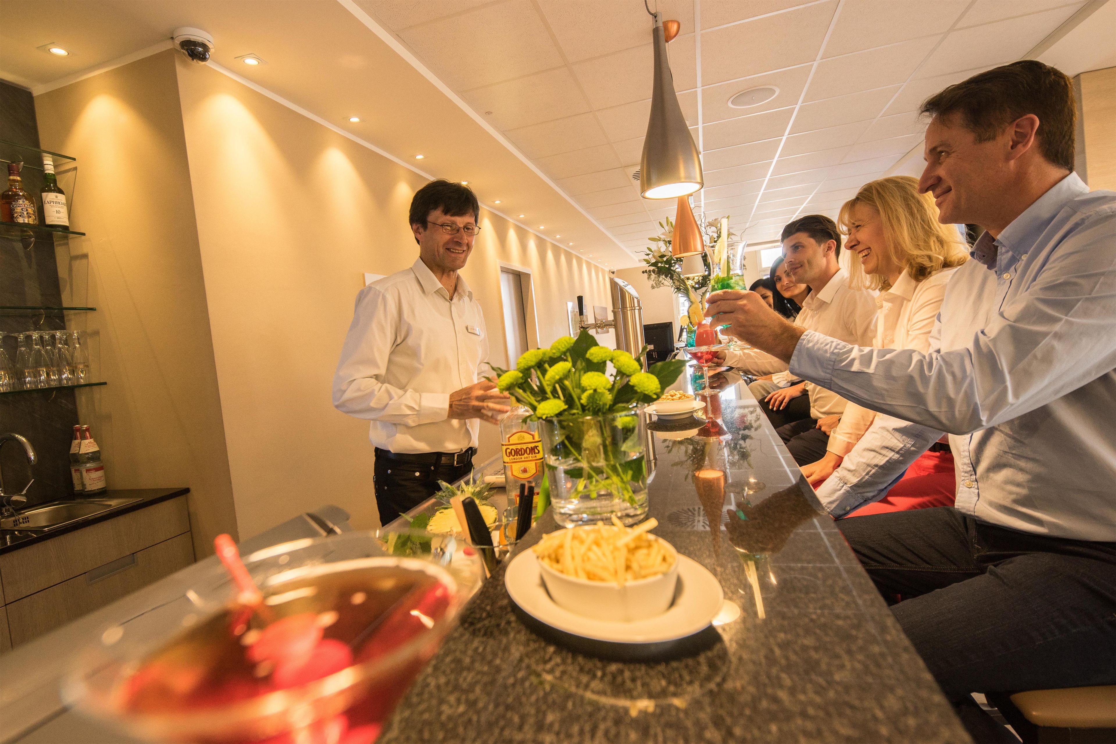 A bar area with a counter, glasses, bottles, and a person pouring a drink.