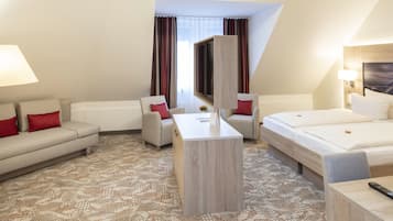 Ein Hotelzimmer mit einer Sitzecke, zwei Sesseln, einem Bett, einem Fernseher und einem Schreibtisch.
