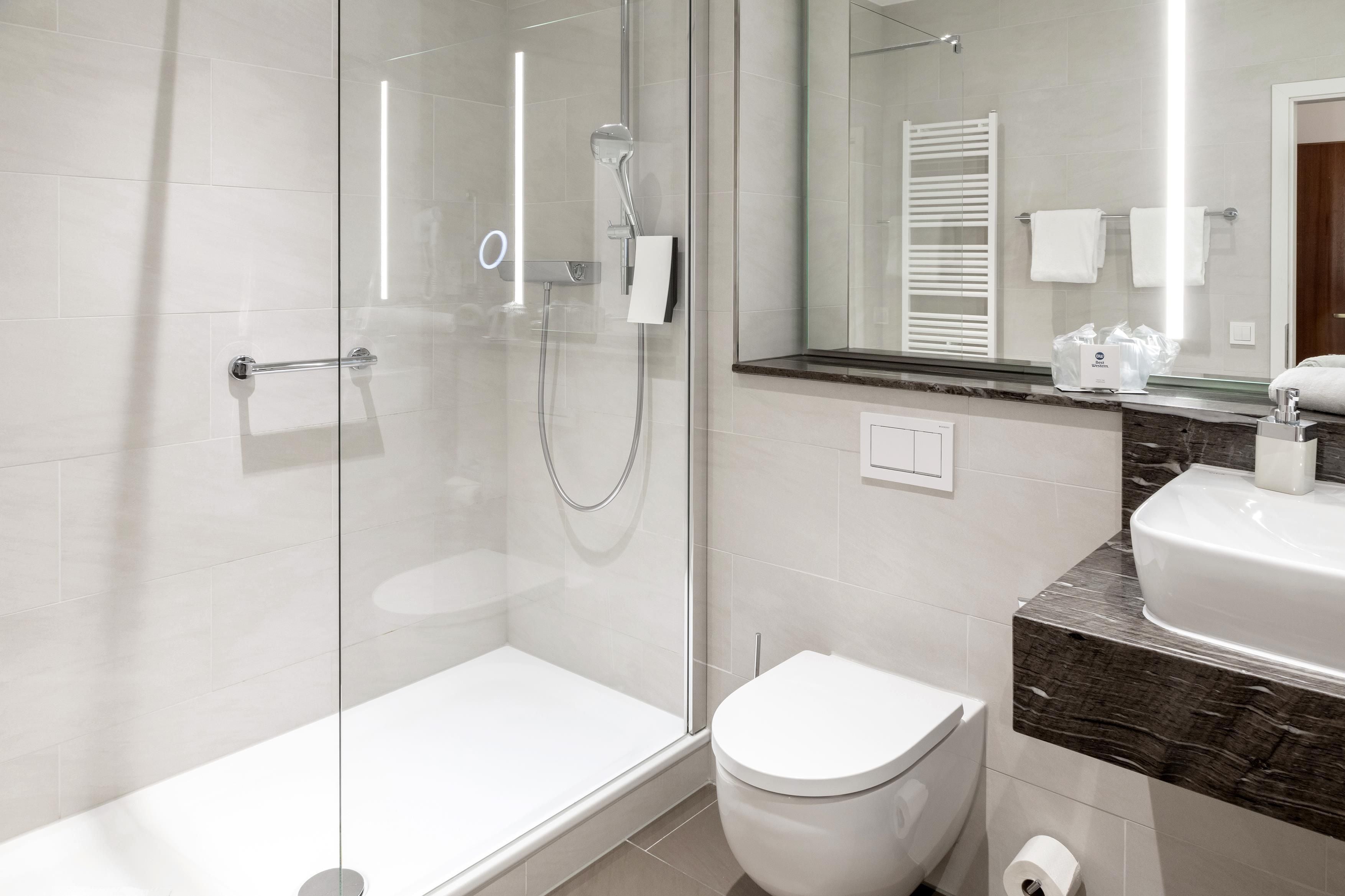 Un baño moderno con ducha envuelta en vidrio, inodoro blanco y lavamanos con encimera de mármol.