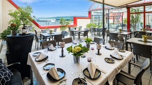 Een dakterrasrestaurant met gedekte tafels, met uitzicht op een stadslandschap.