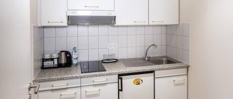 Cocina compacta con gabinetes blancos, encimera de granito, campana extractora integrada, lavamanos y cafetera.