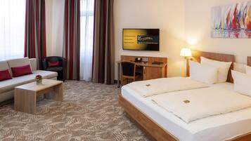A hotel room with a bed, a desk, a chair, a sofa, a TV, and a painting on the wall.