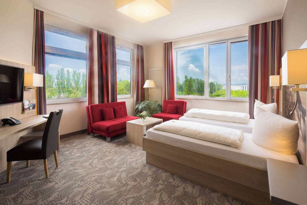 Habitación de hotel con cama, escritorio, una silla y dos sofás rojos.