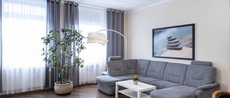 Una sala de estar moderna con un sofá seccional gris, una mesa de centro blanca, una lámpara de pie y una planta en maceta.