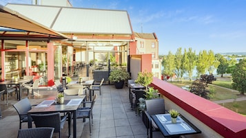 An outdoor patio with tables and chairs, a covered seating area, and a view of a lake and trees.