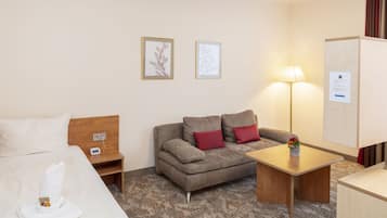 A hotel room with a bed, a sofa, a small table, a lamp, and two framed pictures on the wall.