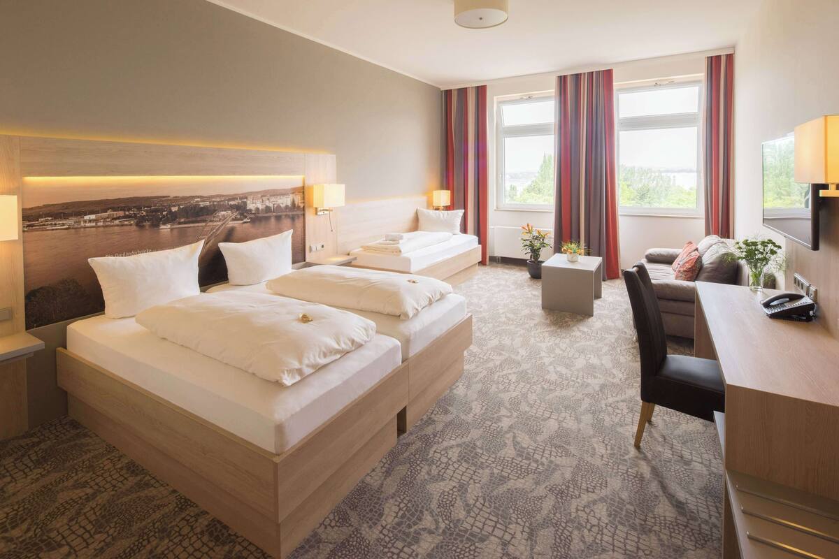 Habitación de hotel con dos camas, un escritorio, una silla, una mesita con una planta y vistas a una masa de agua.