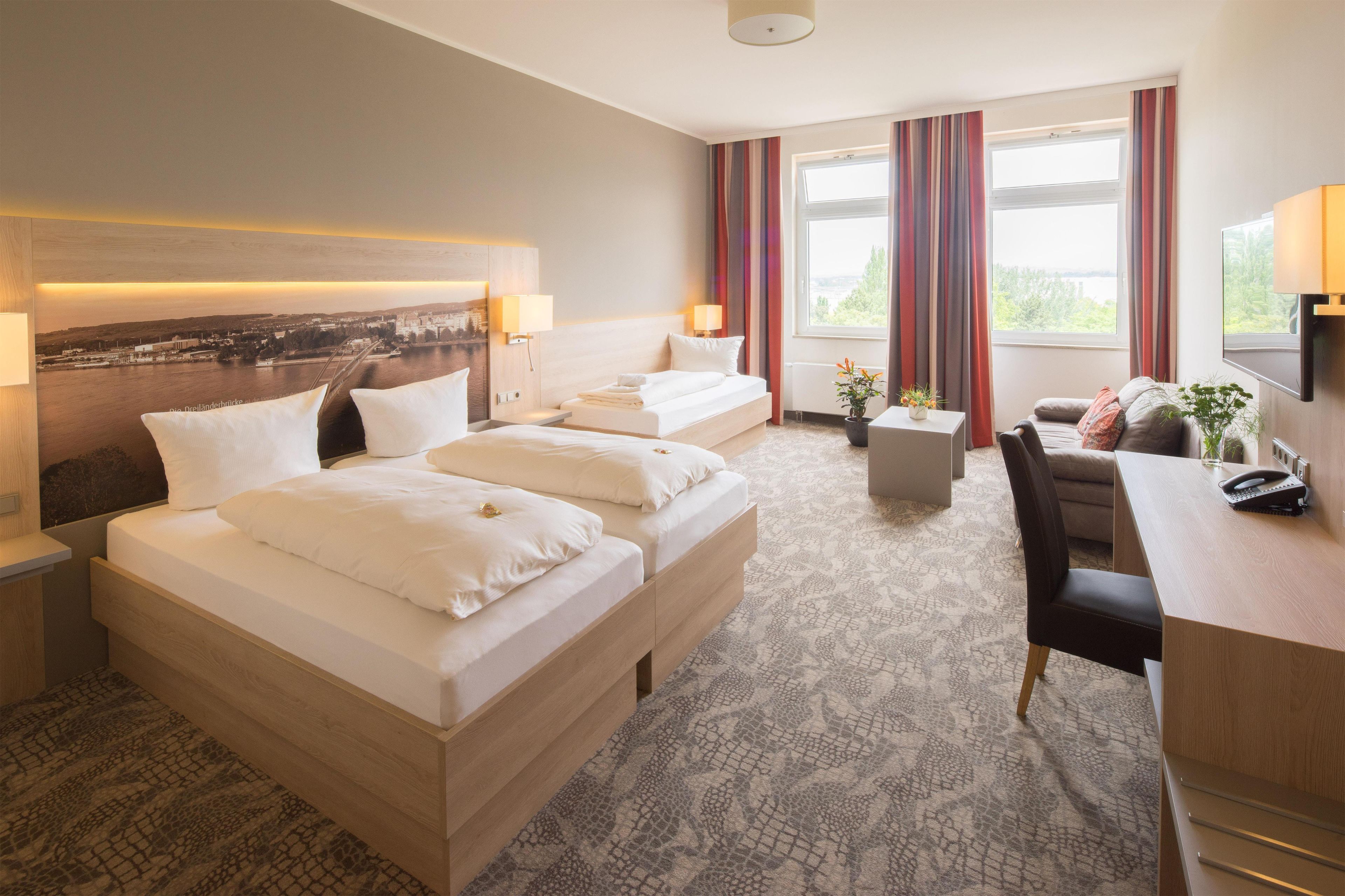 A hotel room with two beds, a desk, a chair, a small table, and a TV.