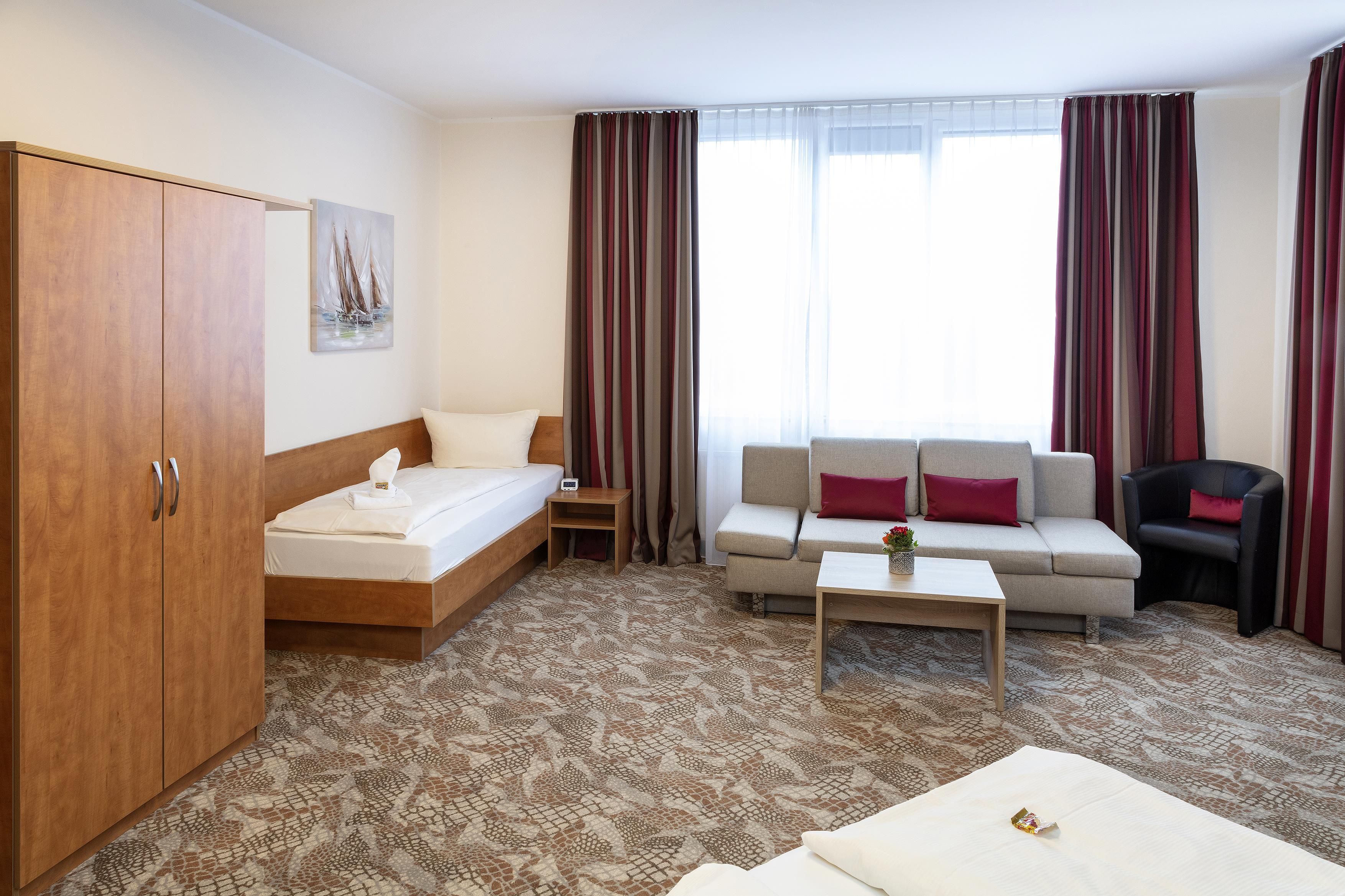 A hotel room with a bed, a sofa, a chair, a coffee table, and a wardrobe.