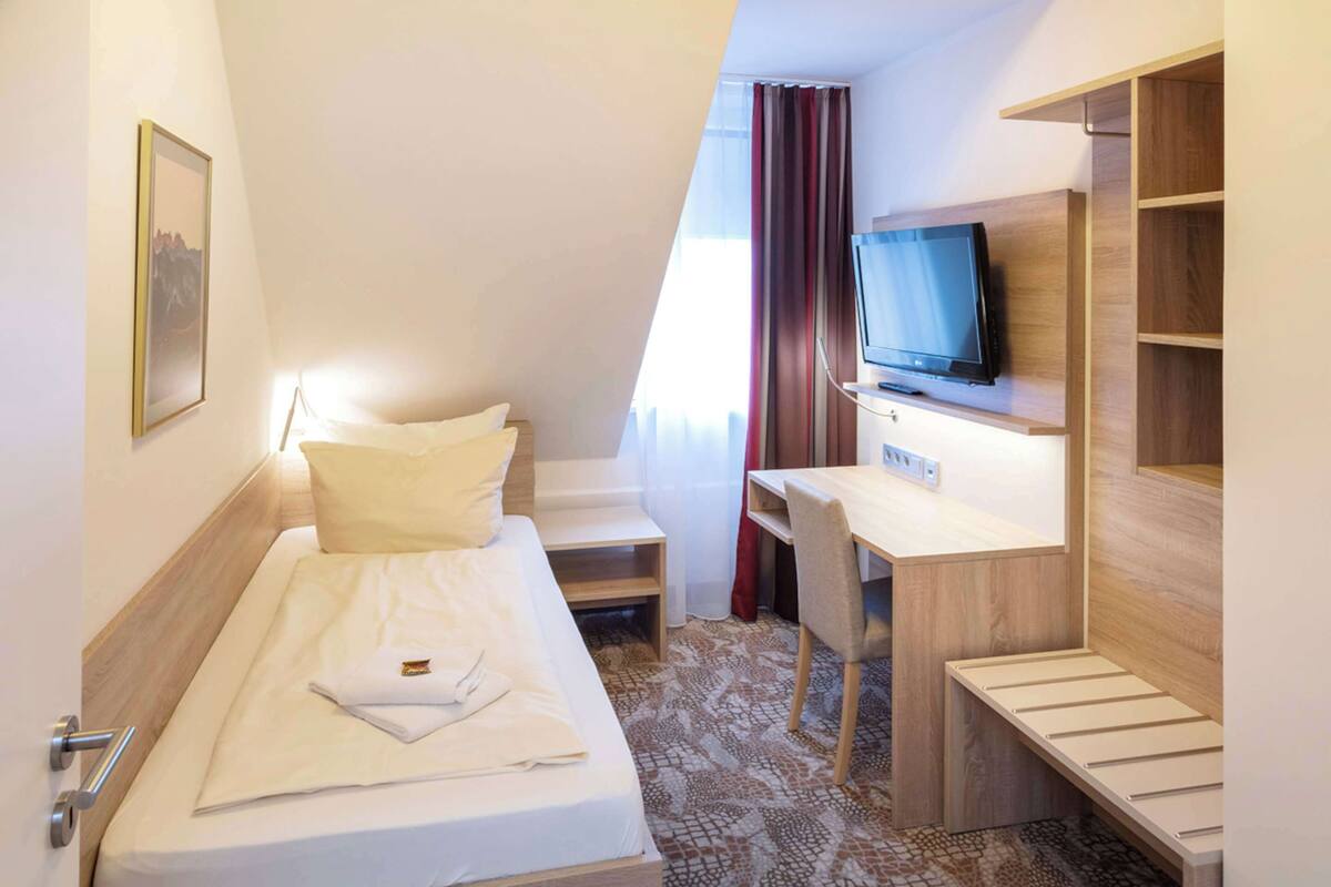 Una habitación de hotel pequeña con cama, escritorio, televisión y un rincón de descanso.