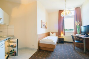 Una habitación de hotel con cama, escritorio, televisión y ventana con cortinas.