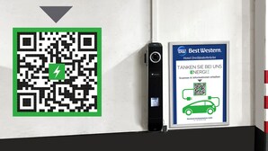 Een QR-code en een digitaal apparaat op een muur, met een bord waarop Best Western Hotel Dreiländerbrücke wordt aangeboden.
