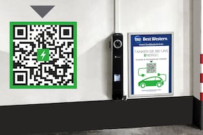 En QR-kode og en digital enhed på en væg, med et skilt der reklamerer for Best Western Hotel Dreiländerbrücke.