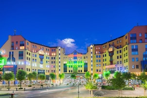 A multi-story hotel with a central entrance, surrounded by a landscaped area with trees and a fountain.