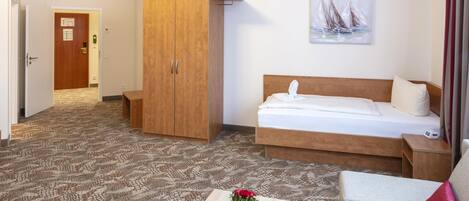Una habitación de hotel con una cama, un armario de madera, una mesita con un jarrón de flores y un cuadro en la pared.