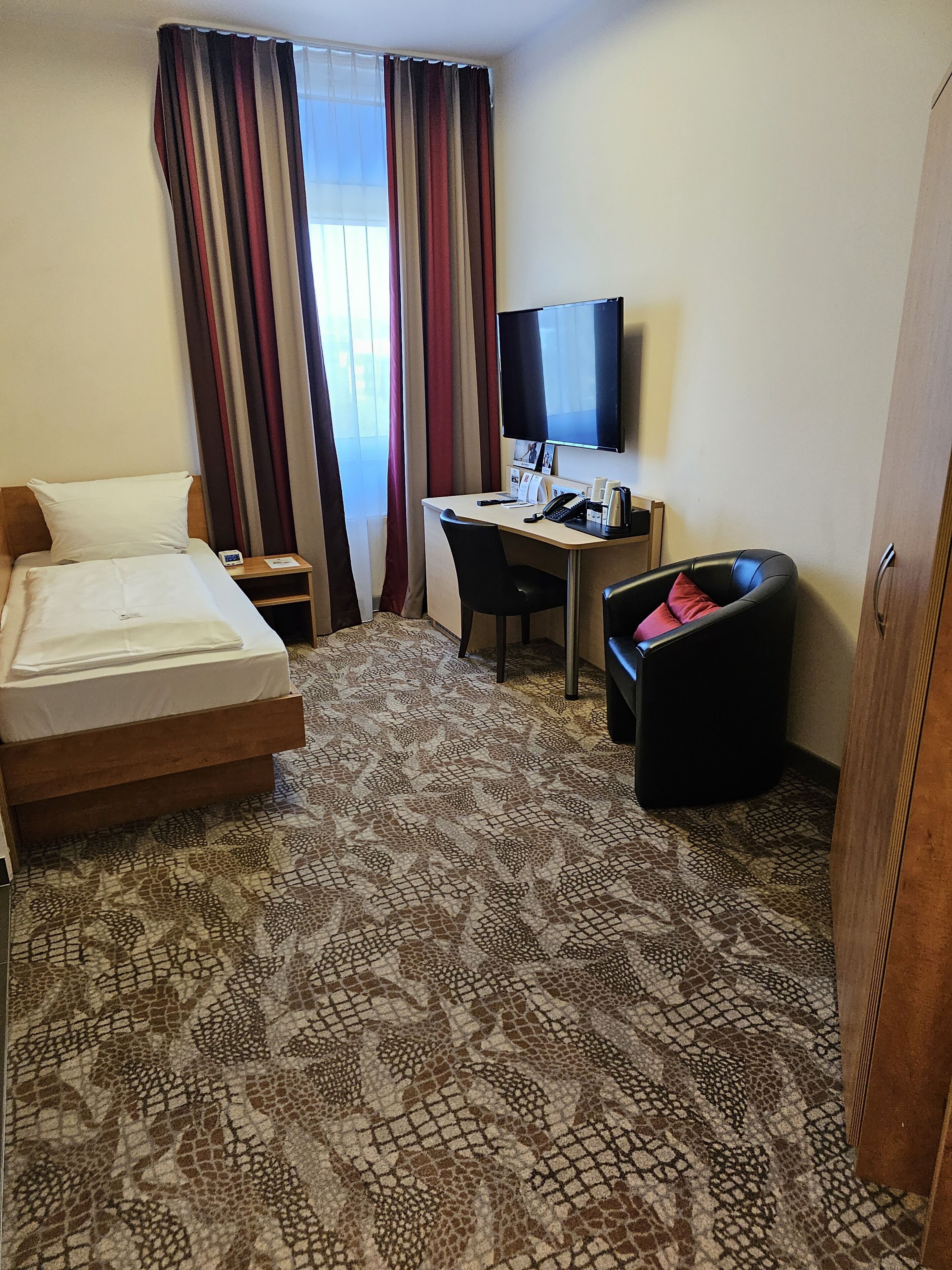 A hotel room with a bed, a desk, a chair, a TV, and a wardrobe.